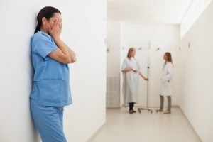 female medical professional leaning against wall with head in hands in hospital corridor