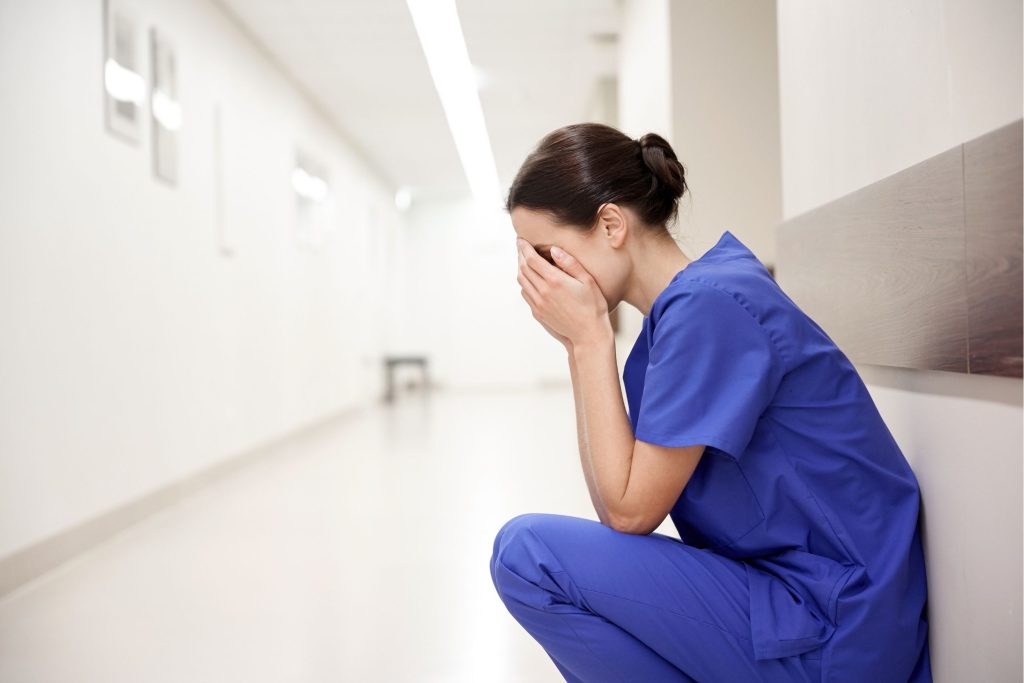 Woman in scrubs covering her face and sitting on the hospital floor
